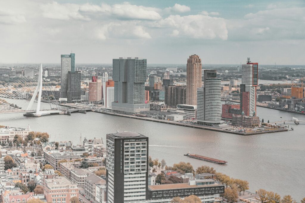 A city skyline with modern high-rises beside a wide river and a white cable-stayed bridge on a cloudy day.