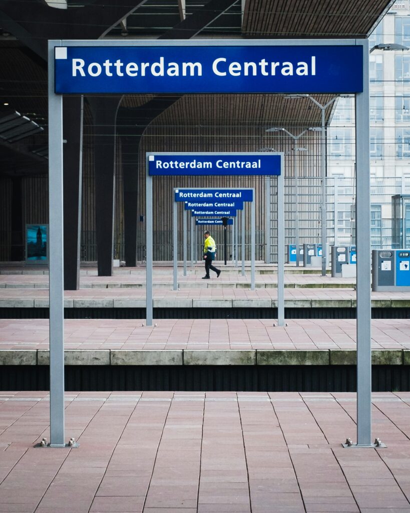 Blue Rotterdam Centraal signs repeat in perspective at a train station, with a person in yellow walking.