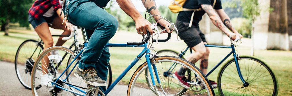 Three people riding bicycles together outdoors on a sunny day, with trees and grass in the background.