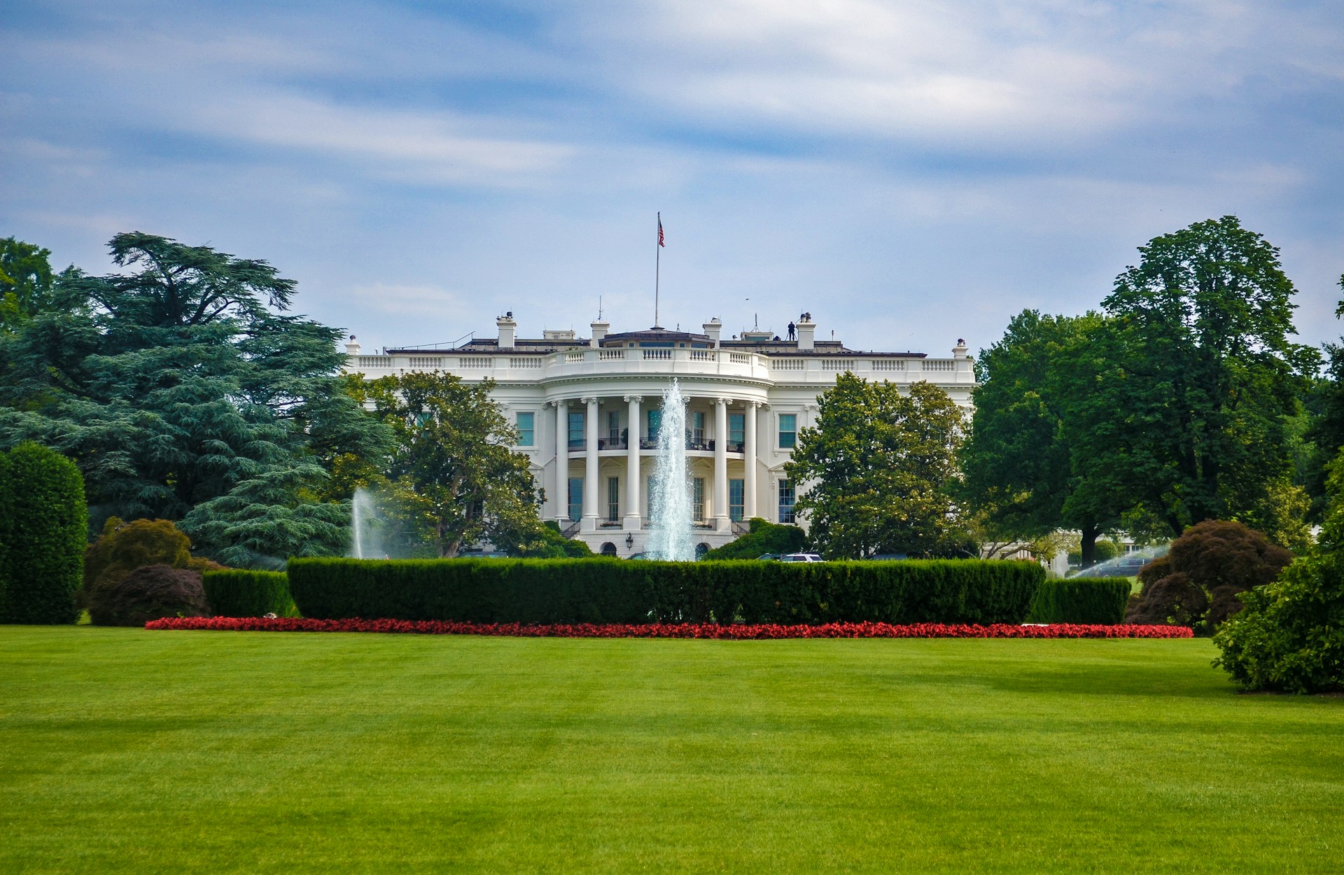 The White House south facade with fountain, manicured lawn and red flower beds in Washington DC