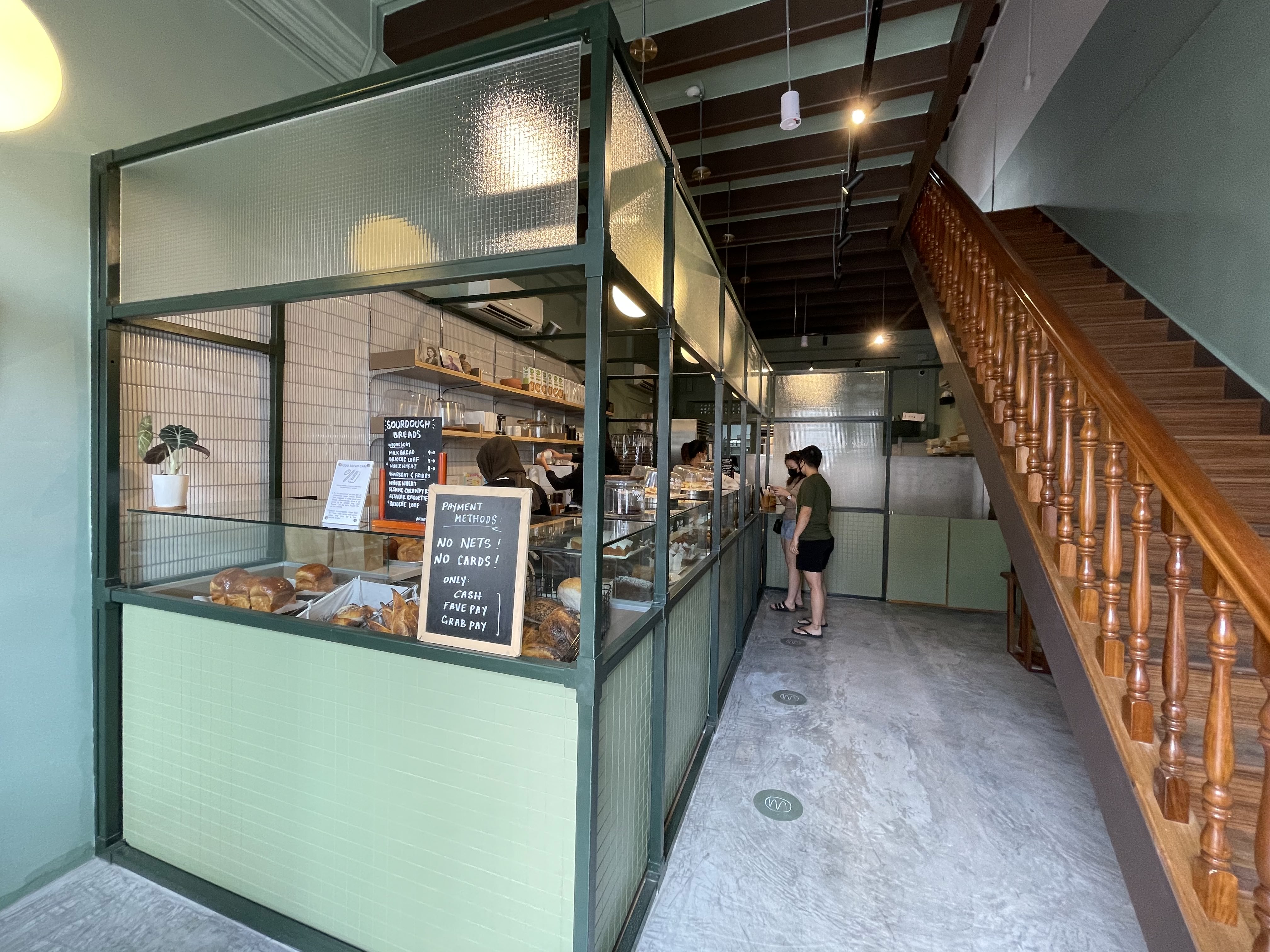 Interior of Mother Dough bakery in Kampong Glam, Singapore, with a glass-fronted pastry case, sage-green fittings and a wooden staircase