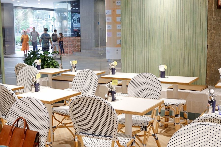 Little Farms cafe seating in Singapore with white polka-dot bistro chairs, light wood tables and a green wall by a mall walkway