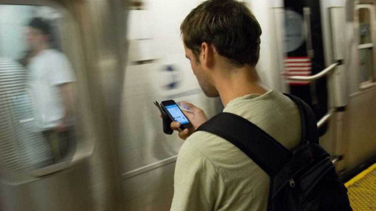 Business traveler with a backpack checking a navigation app on his phone while waiting on a subway platform