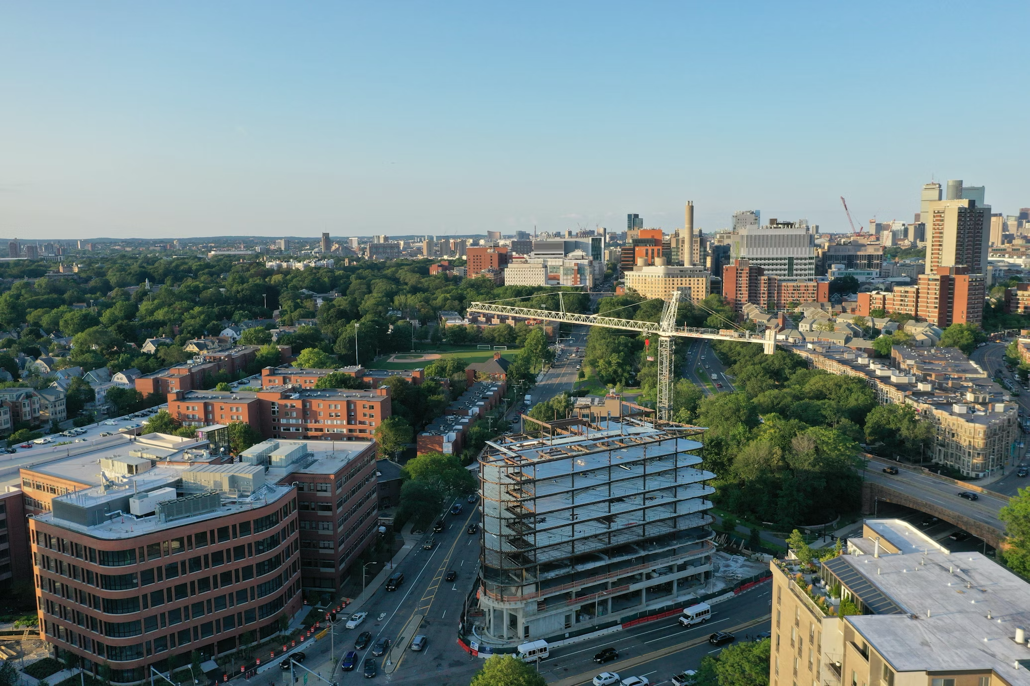 Aerial view of a Boston neighborhood with tree-lined streets, brick buildings and the skyline beyond