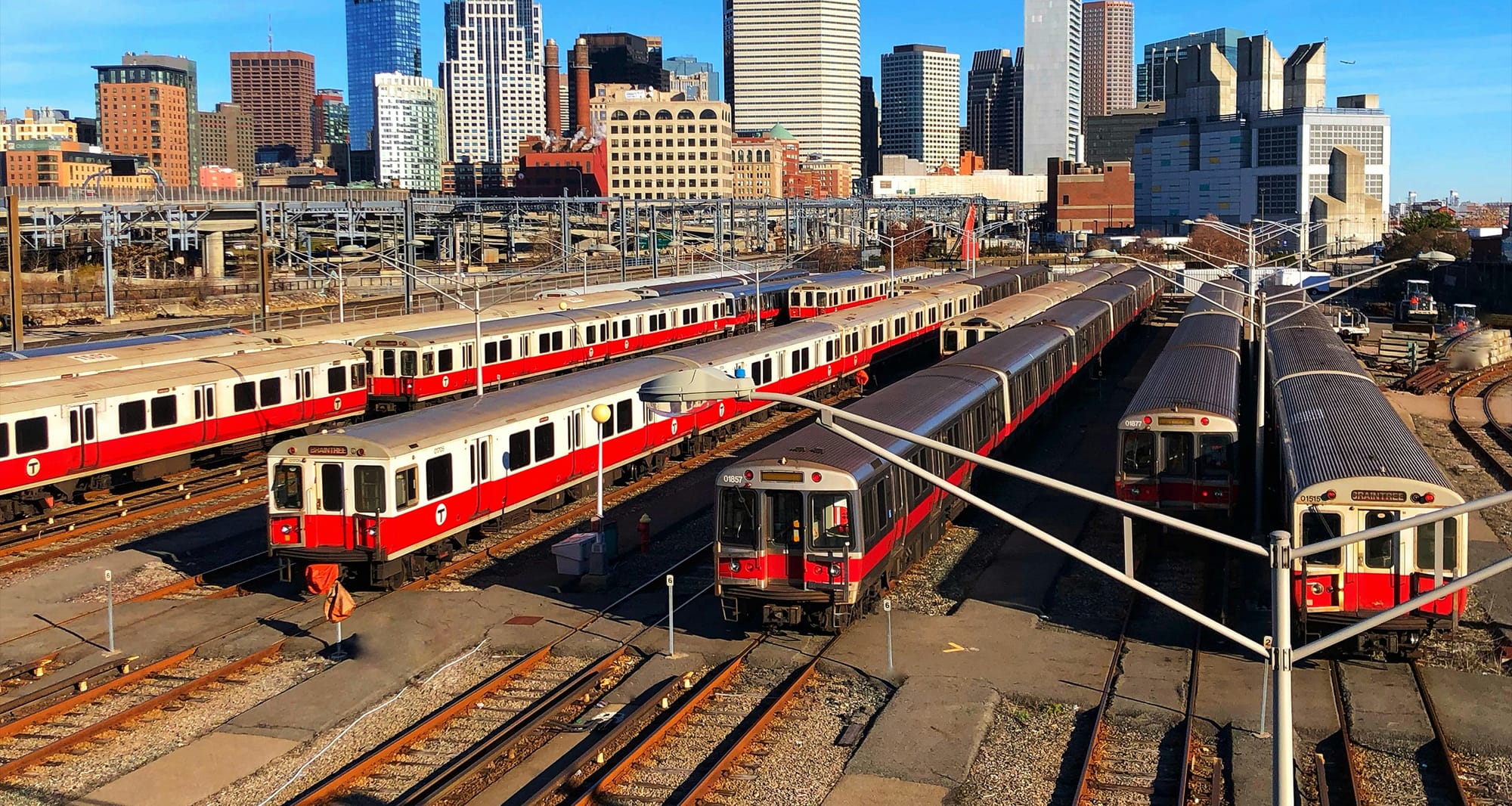 Boston MBTA Red Line subway cars parked in a rail yard with the downtown skyline behind