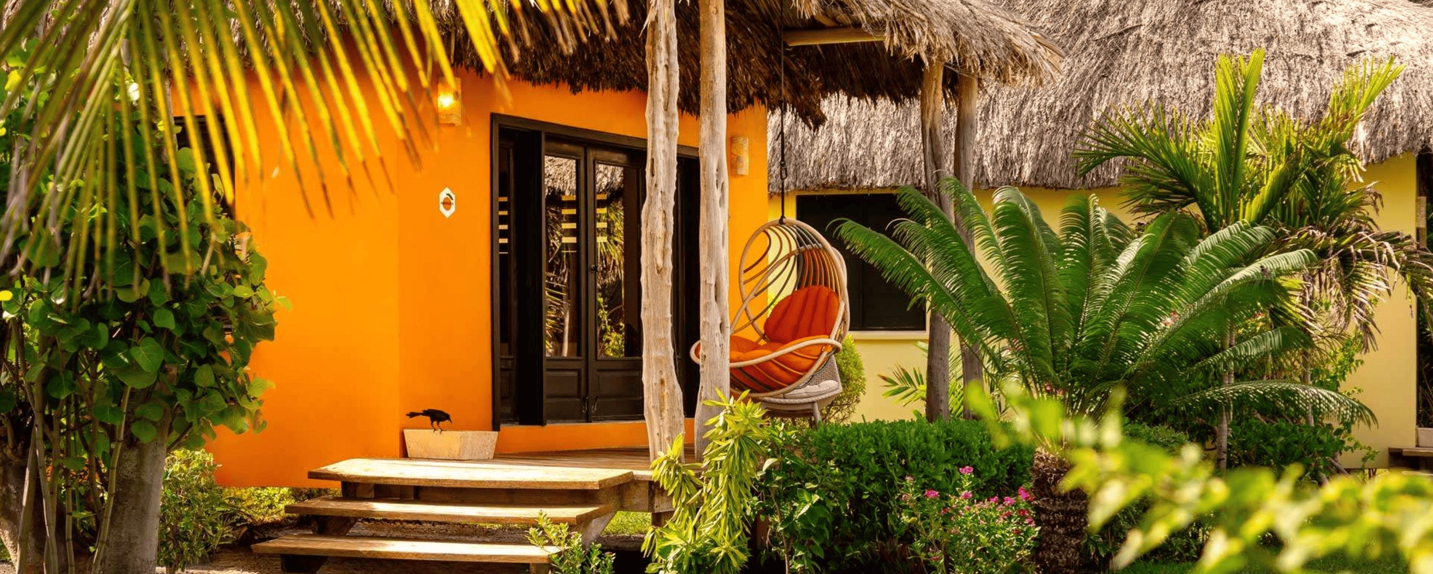 Orange thatched-roof casita with a hanging chair, wooden steps and lush palms at a resort on Ambergris Caye, Belize