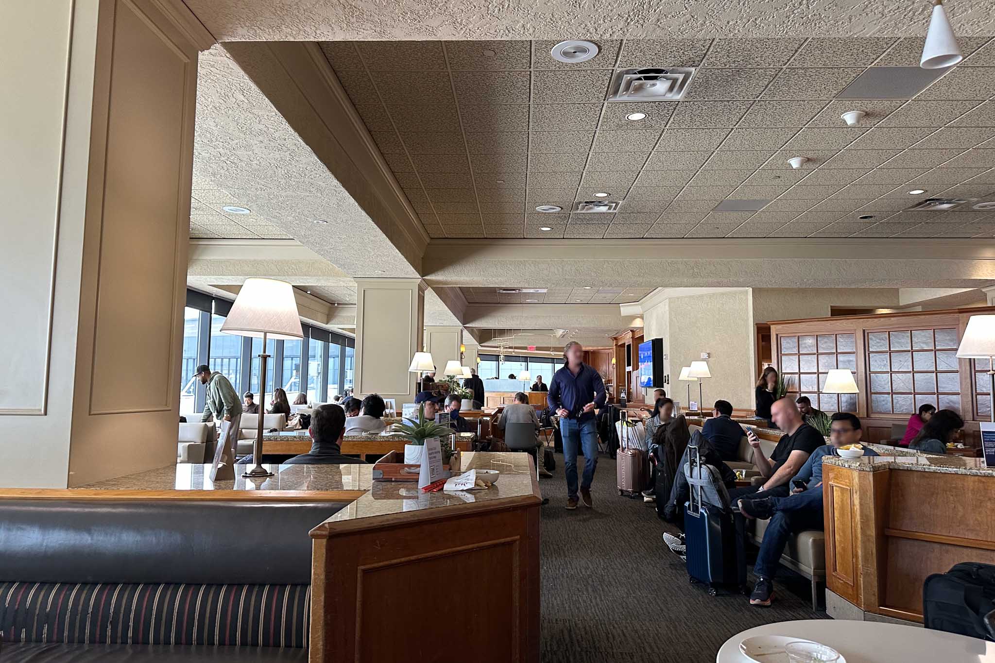 Busy airport lounge interior with travelers seated among lamps, dividers and luggage