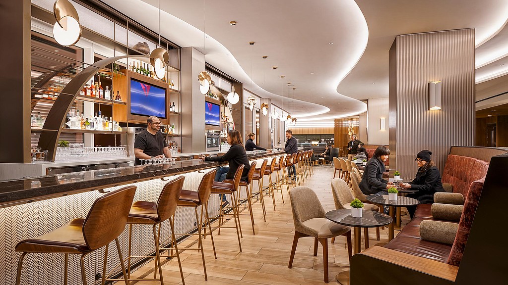 Sustainable airport lounge bar with curved ceiling, pendant lights and guests seated at the counter