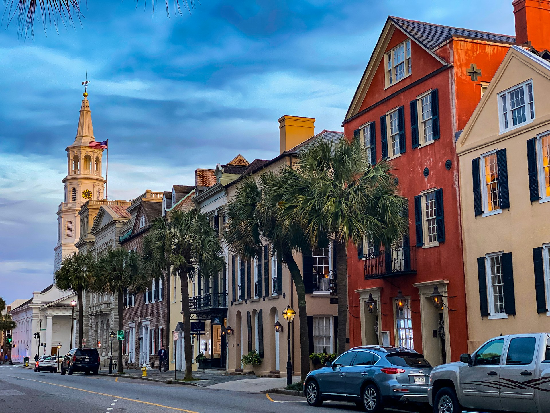 Colorful historic row houses, palm trees and a church steeple along a Charleston street at dusk