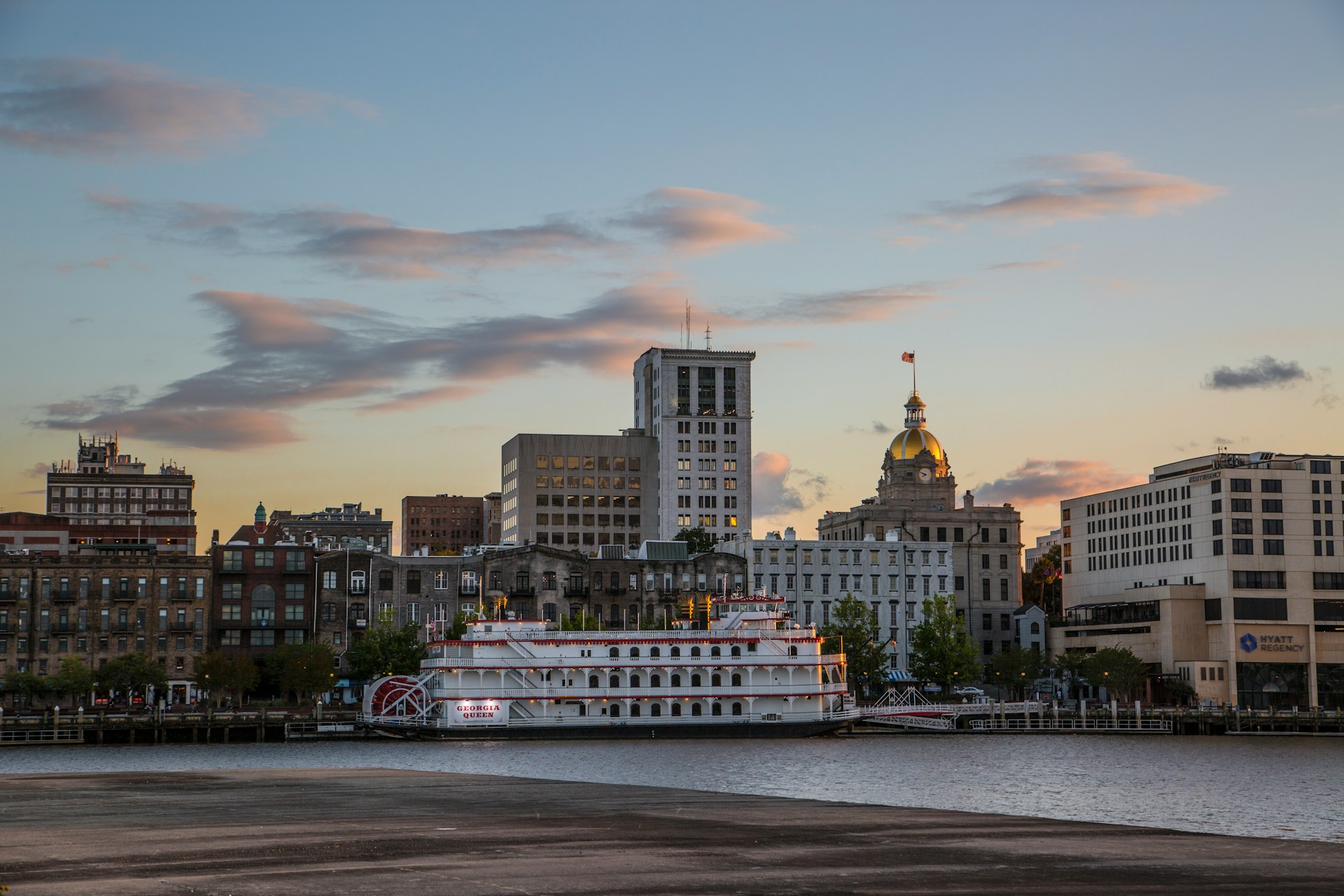 Savannah riverfront at dusk with the Georgia Queen paddlewheel riverboat and the gold-domed city hall in the skyline