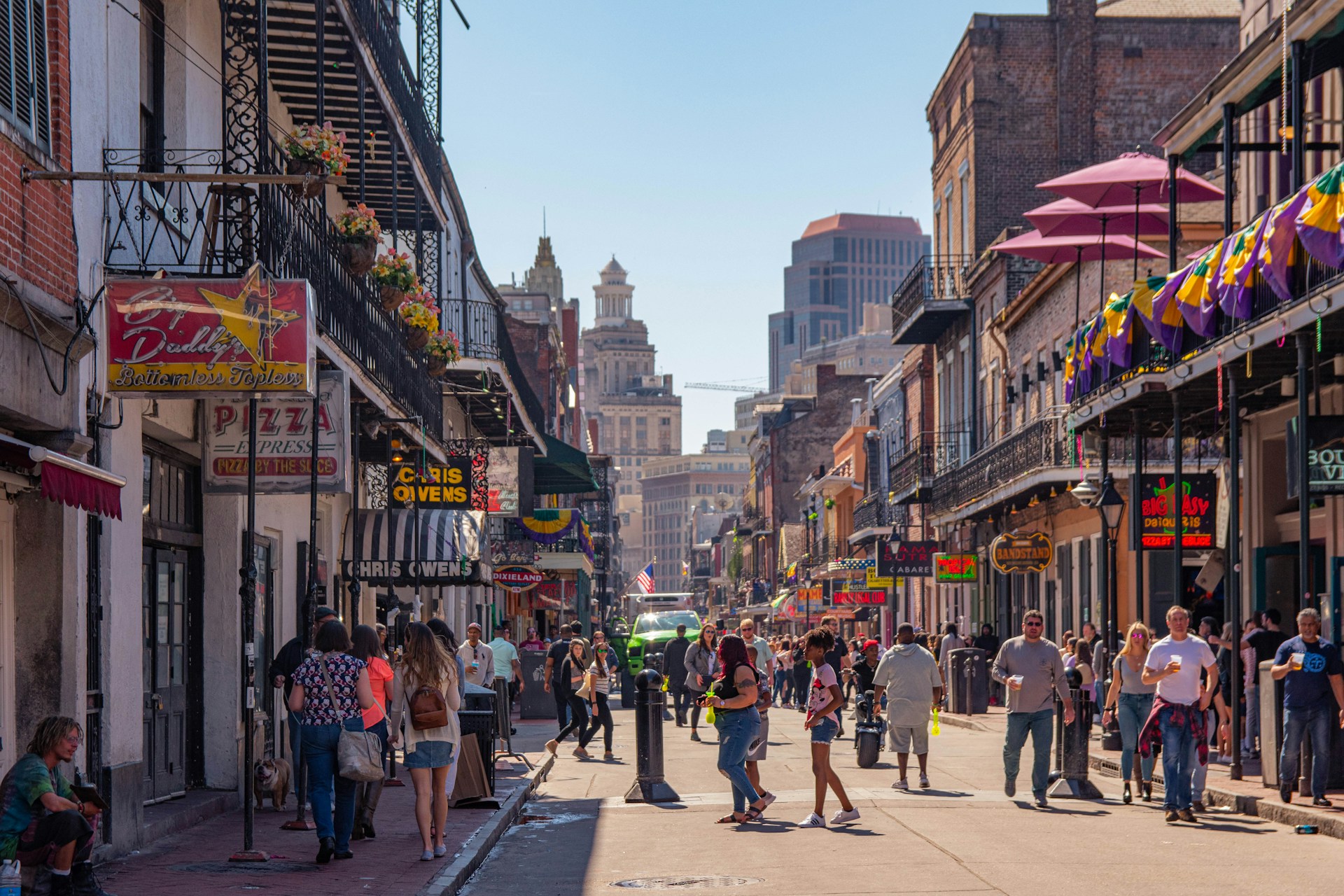Crowds walking Bourbon Street in the New Orleans French Quarter past colorful balconies and neon signs