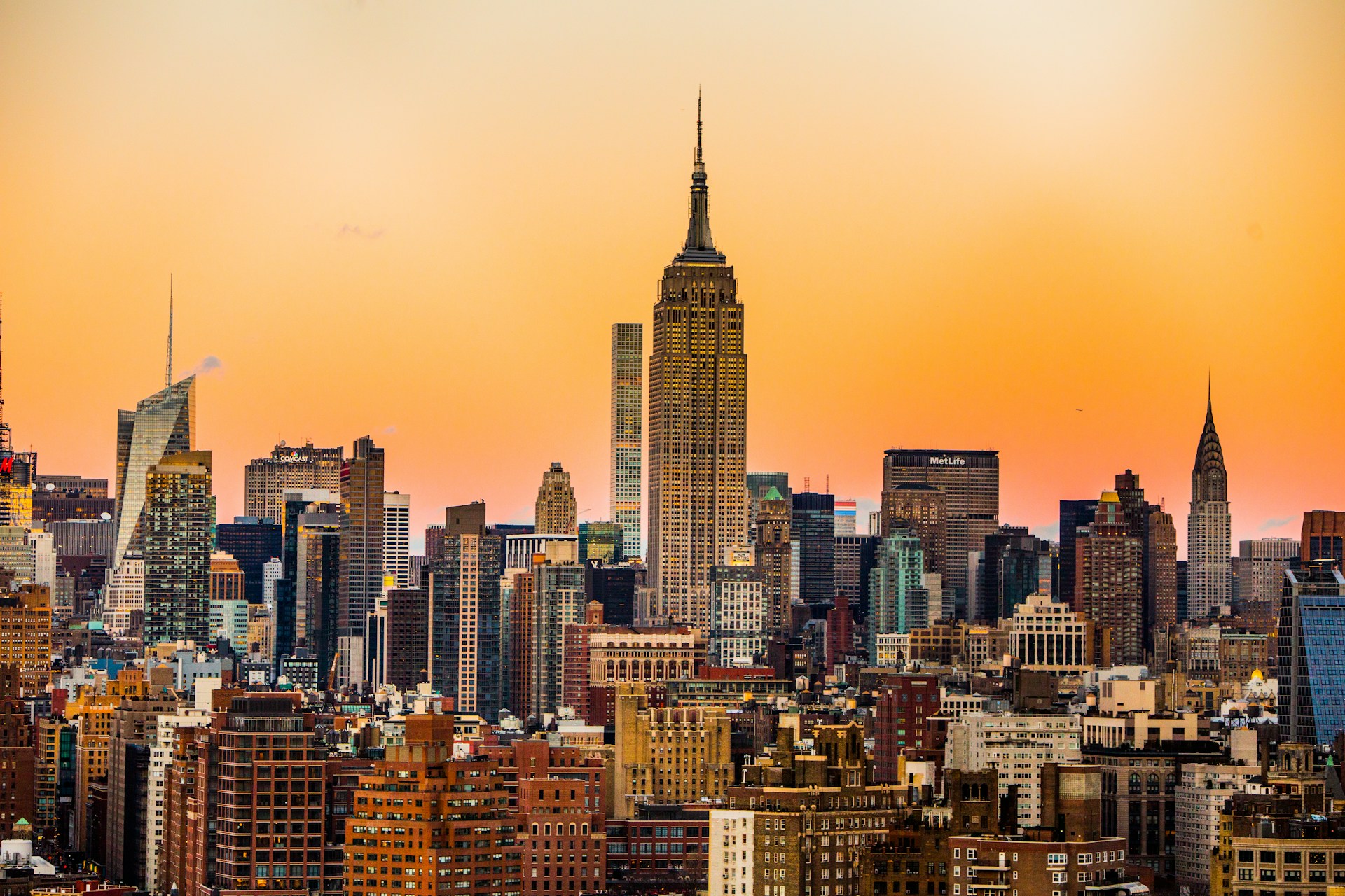 New York City skyline at sunset with the Empire State Building and Chrysler Building against an orange sky