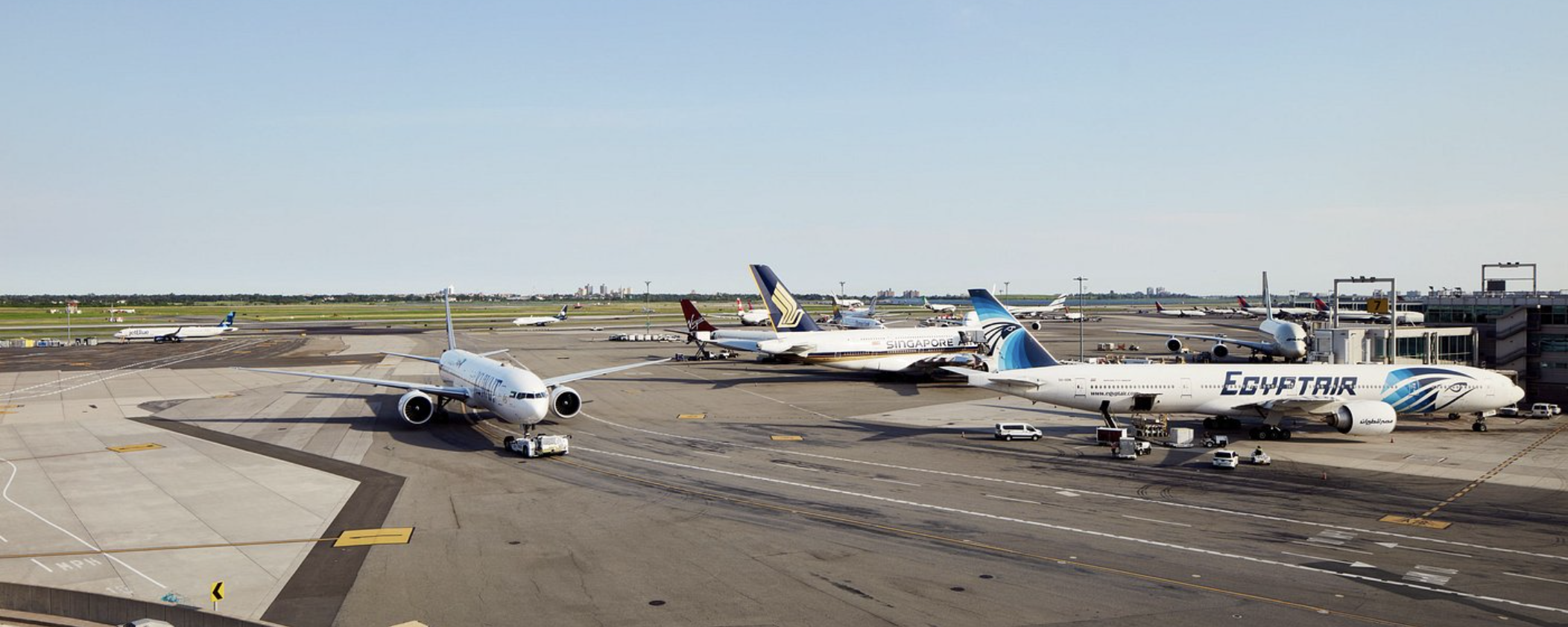 Aircraft including an EgyptAir jet parked at gates on the tarmac at JFK Airport under a clear sky