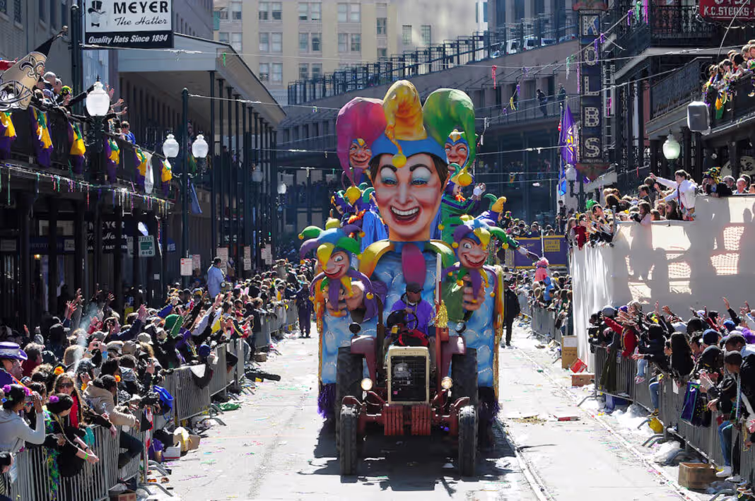 A colorful jester-themed Mardi Gras parade float moving down a crowded New Orleans street
