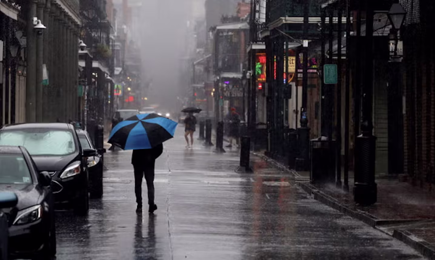 A person with a blue umbrella walking down a rainy, empty New Orleans street during hurricane season
