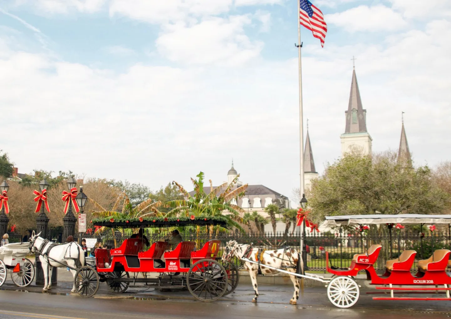 Red horse-drawn carriages with festive holiday wreaths on Jackson Square in winter New Orleans, St Louis Cathedral spires behind