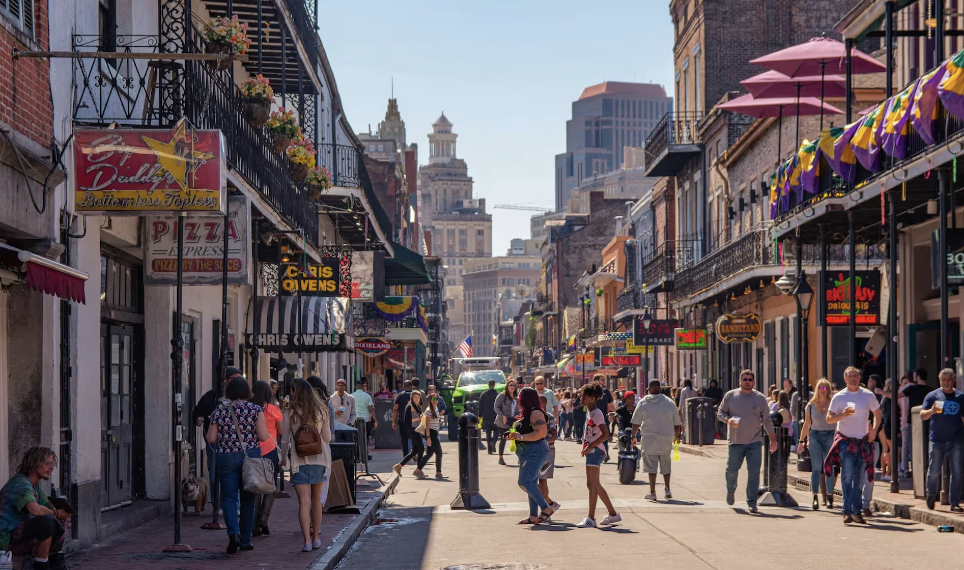 Bourbon Street in New Orleans busy with people, balconies and neon signs in summer light