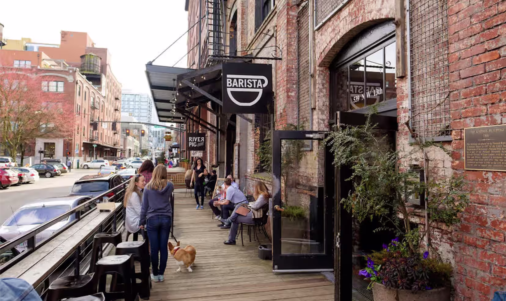 People sitting and walking along a brick-warehouse sidewalk with a Barista cafe in Portland's Pearl District