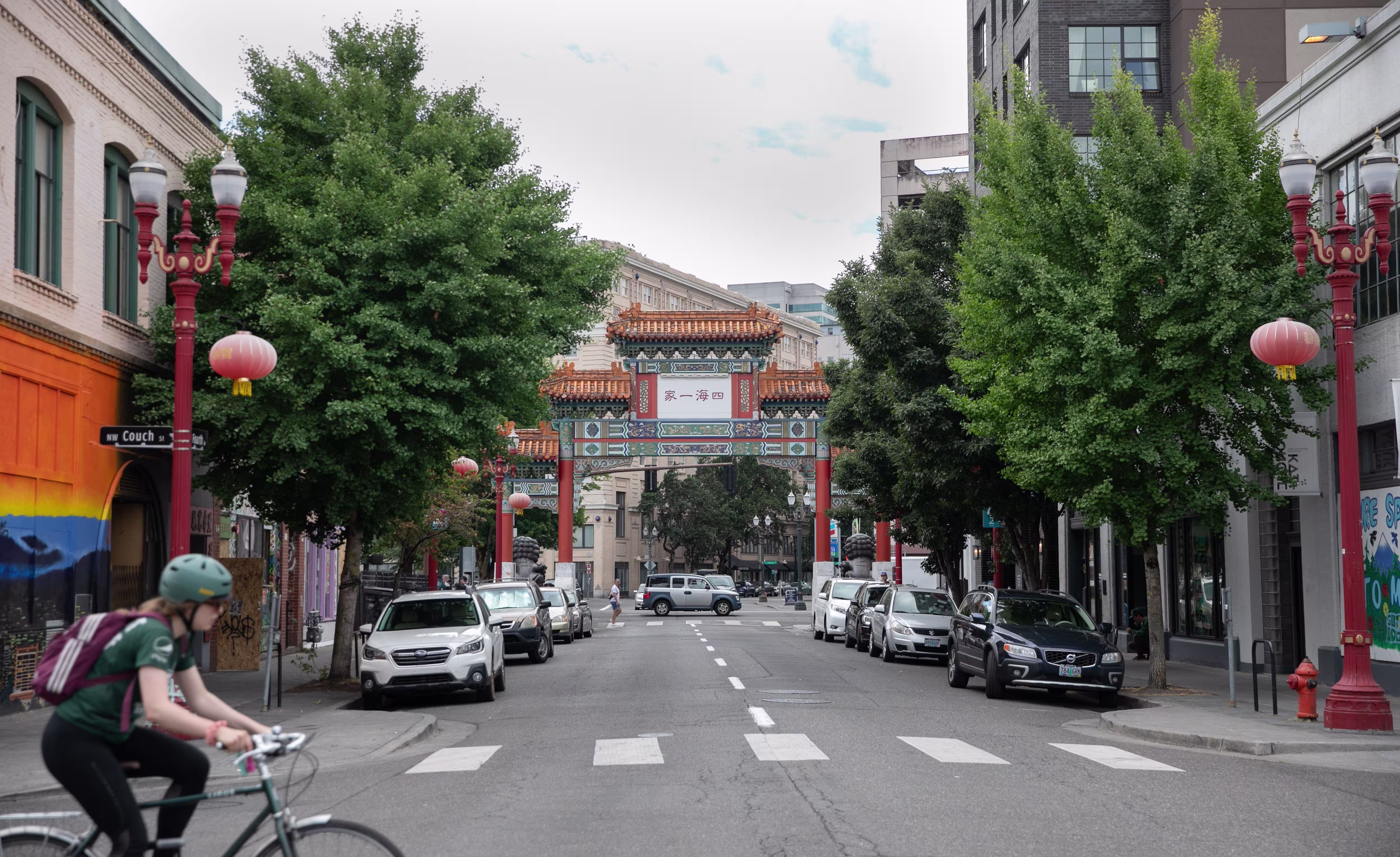 A cyclist crosses a tree-lined street facing the ornate Chinatown gate in Portland's Old Town Chinatown