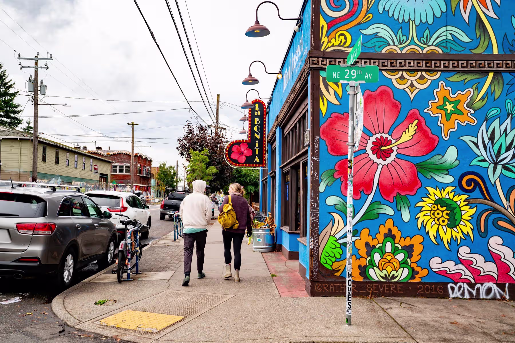 Pedestrians walking past a vivid floral mural on a corner shop in Portland's Alberta Arts District