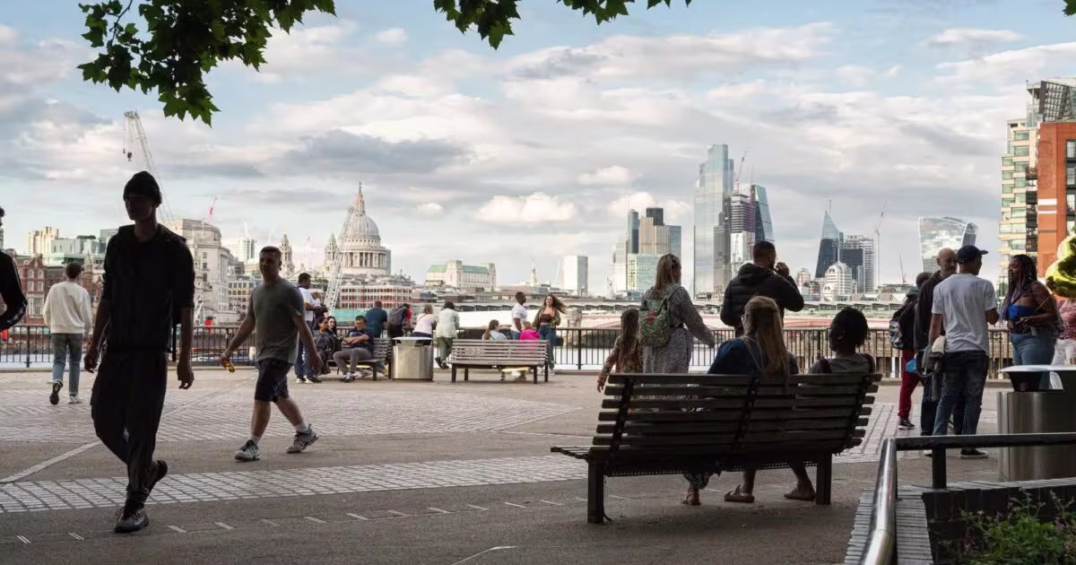 People walking and sitting on a South Bank riverside promenade with the London skyline beyond