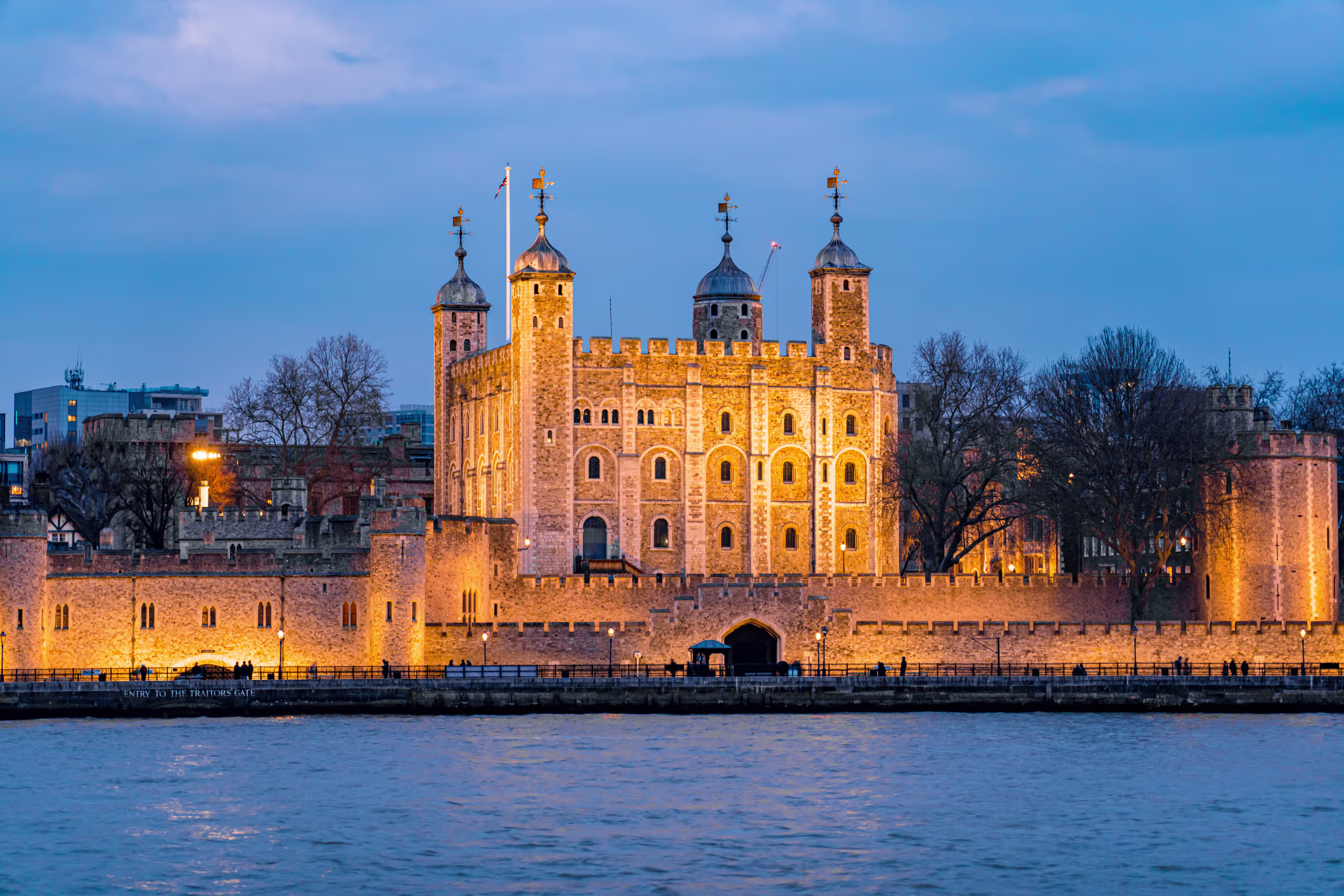 The Tower of London floodlit at dusk along the River Thames