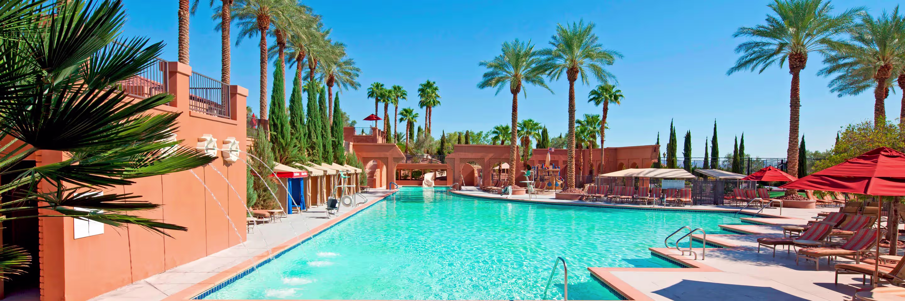 Resort swimming pool lined with palm trees, lounge chairs and red umbrellas at a Las Vegas hotel