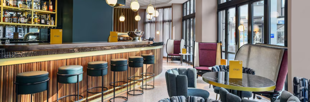 Modern bar with round stools, cozy lounge chairs, and large windows letting in natural light.