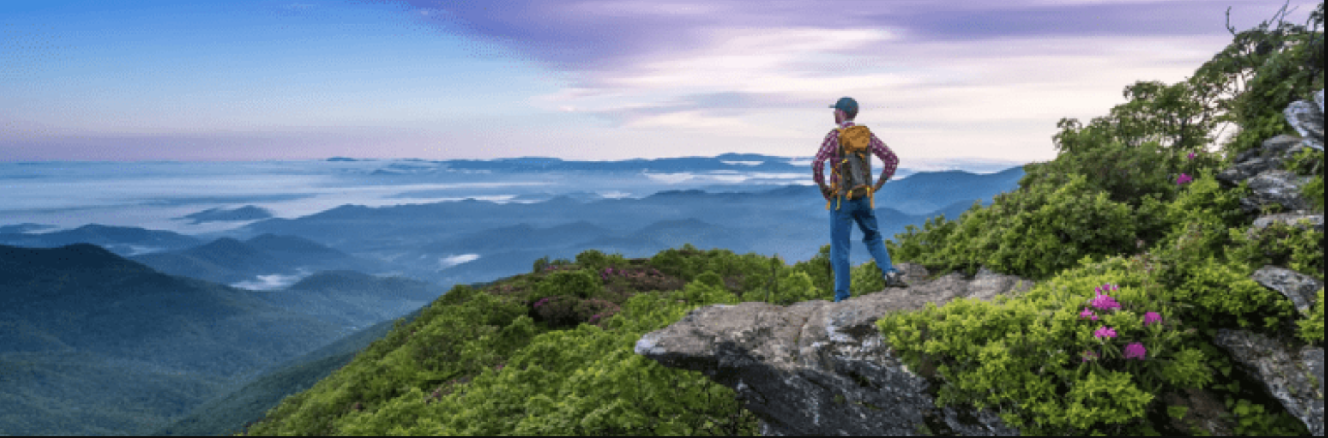 Hiker standing on a rocky mountain summit overlooking layered blue ridges at dawn