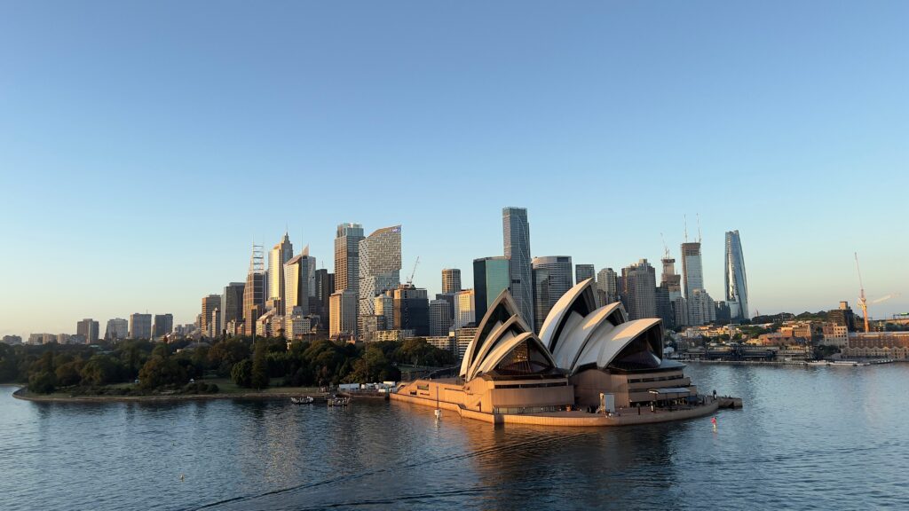 Sydney Opera House with city skyline and waterfront at sunset.