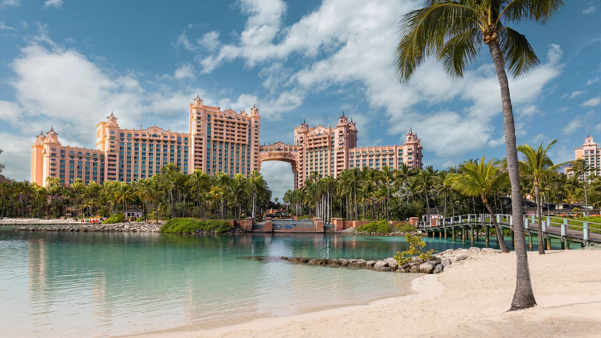 Atlantis Paradise Island resort in the Bahamas seen from a sandy beach with palm tree and turquoise lagoon
