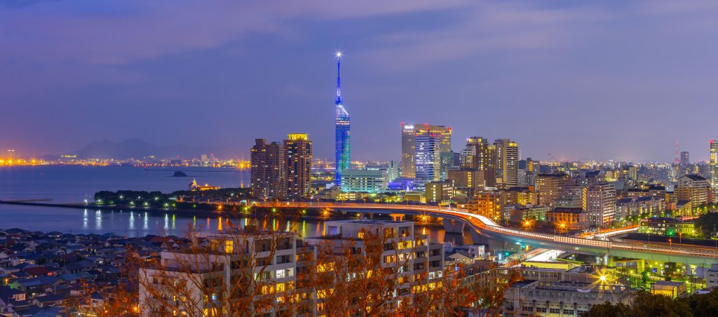 Fukuoka, Japan skyline at dusk with the illuminated Fukuoka Tower, lit city buildings, a river and the bay in the distance