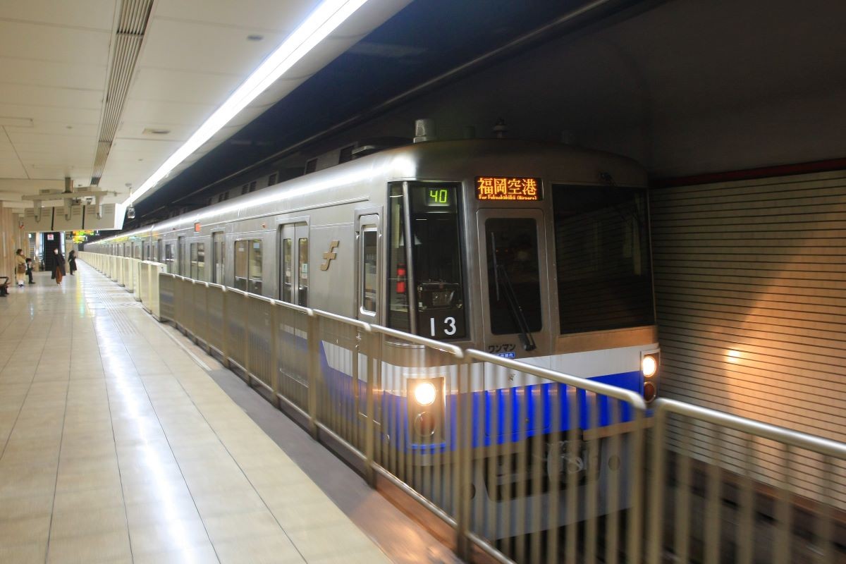 Fukuoka City Subway train arriving at an underground platform, destination sign reading For Fukuoka Airport