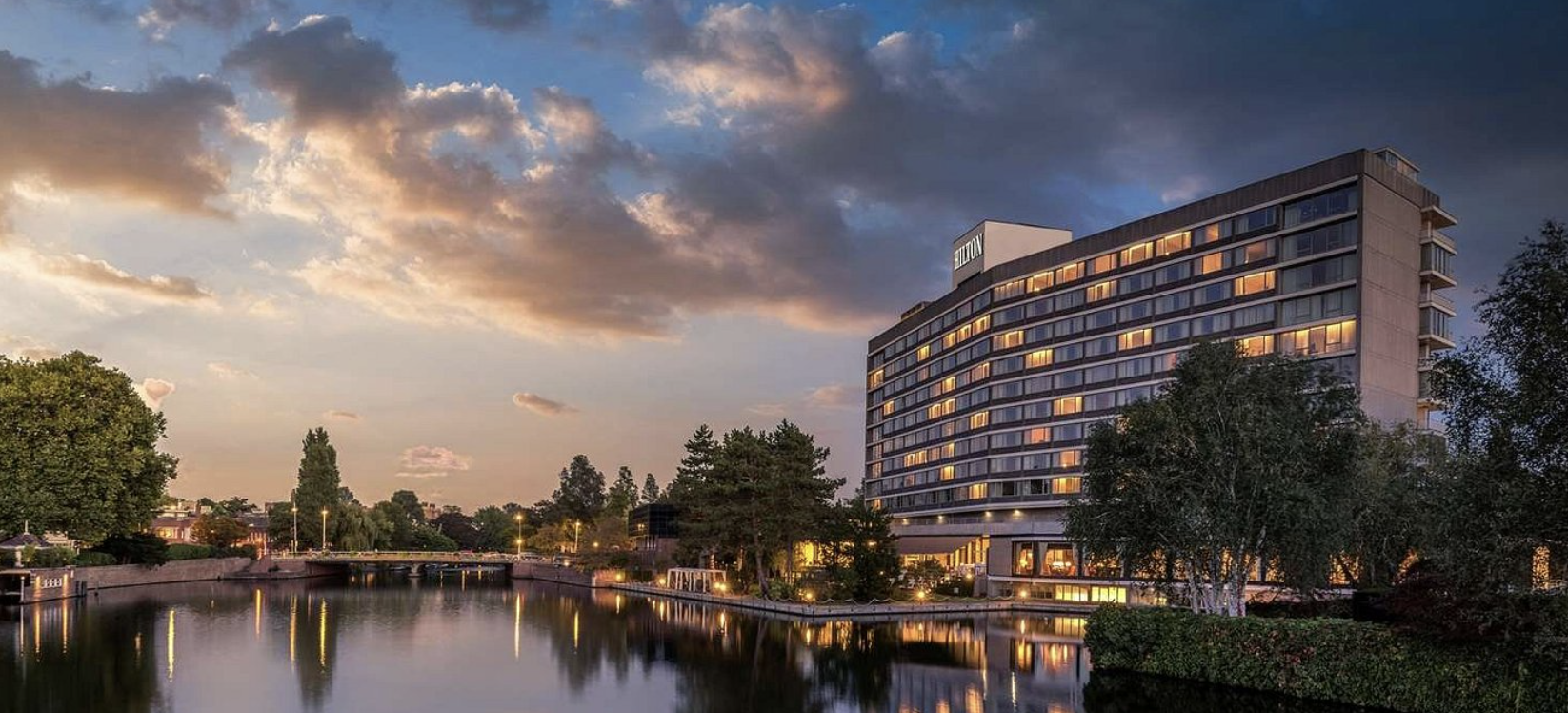 Pestana Amsterdam Riverside hotel at dusk, low-rise building reflected in the river with trees alongside