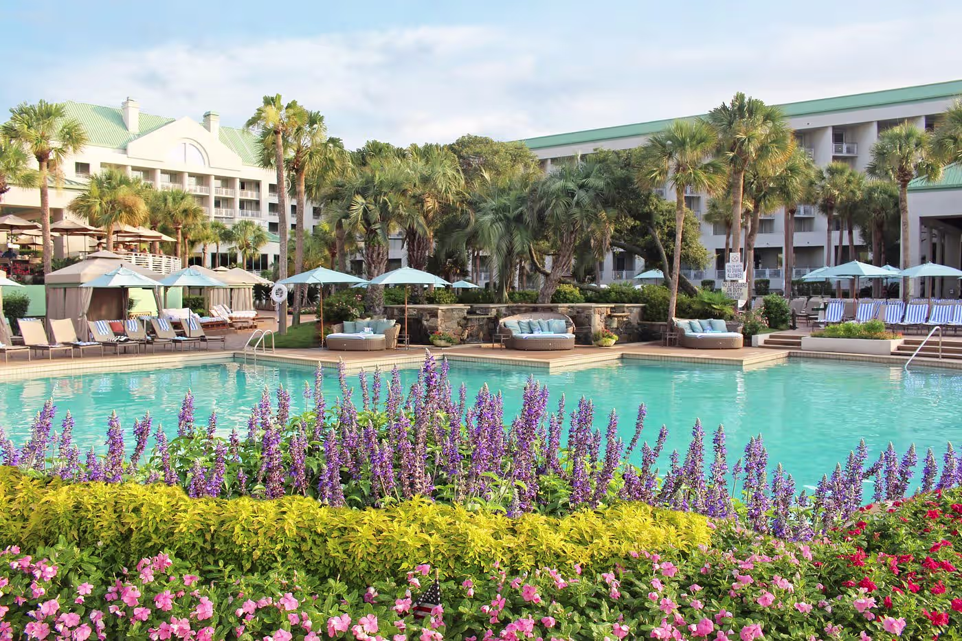 Hilton Head Island resort pool ringed by palms and purple and pink flower beds with loungers and umbrellas