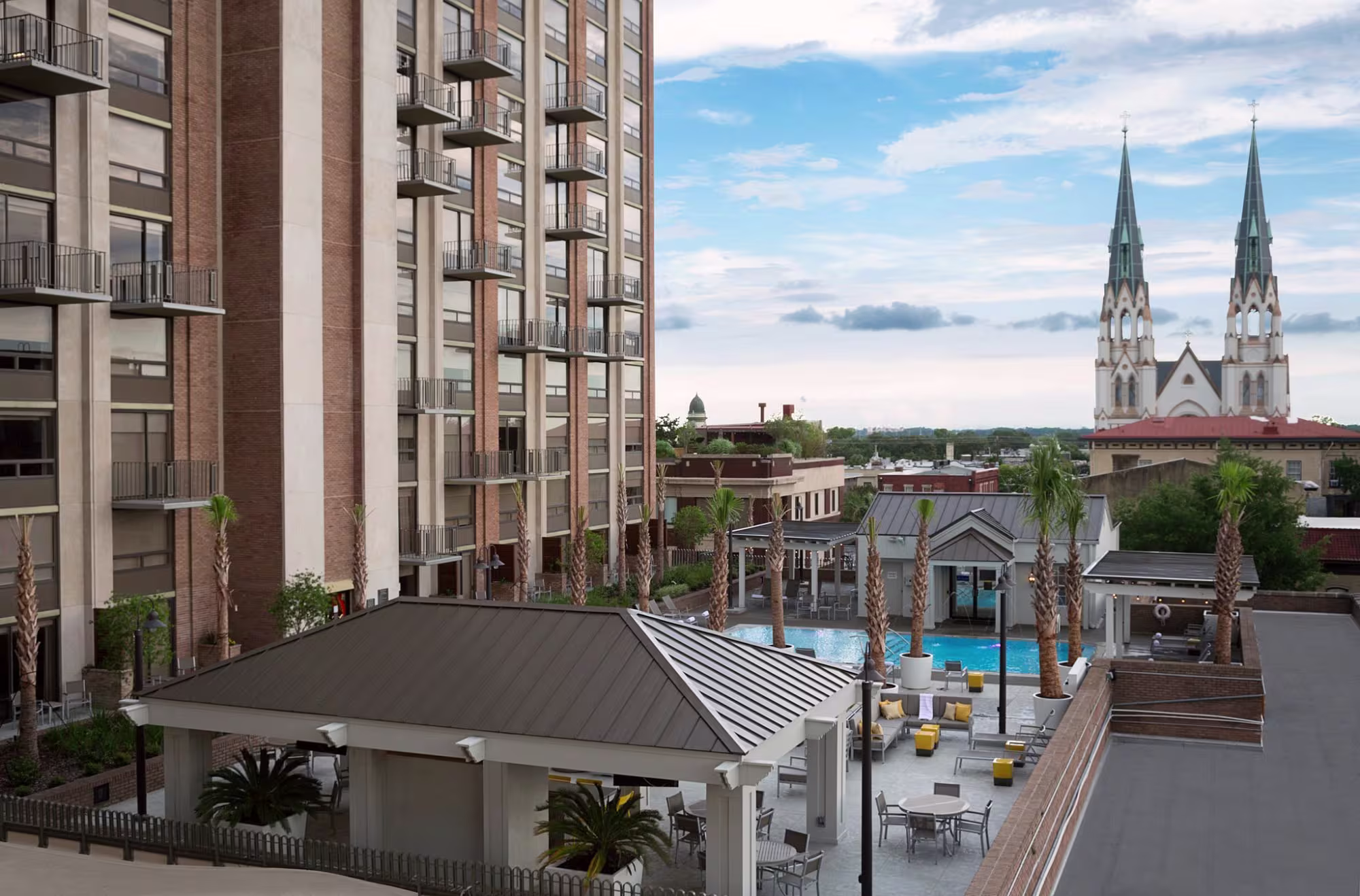 Rooftop pool and patio of a Savannah hotel with the twin spires of the Cathedral of St. John the Baptist beyond
