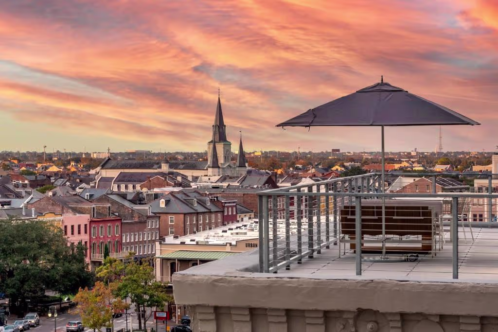 Rooftop terrace with bench and umbrella overlooking the New Orleans skyline and a church spire at sunset