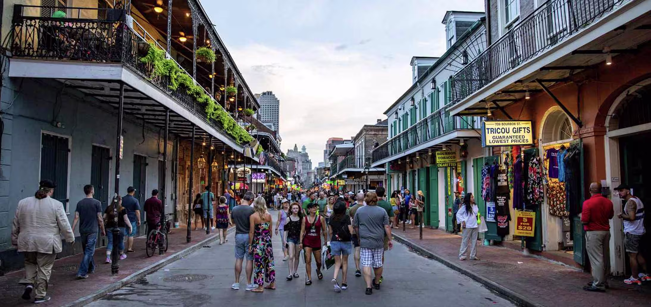 Crowds strolling a French Quarter street in Charleston-style historic district lined with iron-balcony buildings and gift shops at dusk