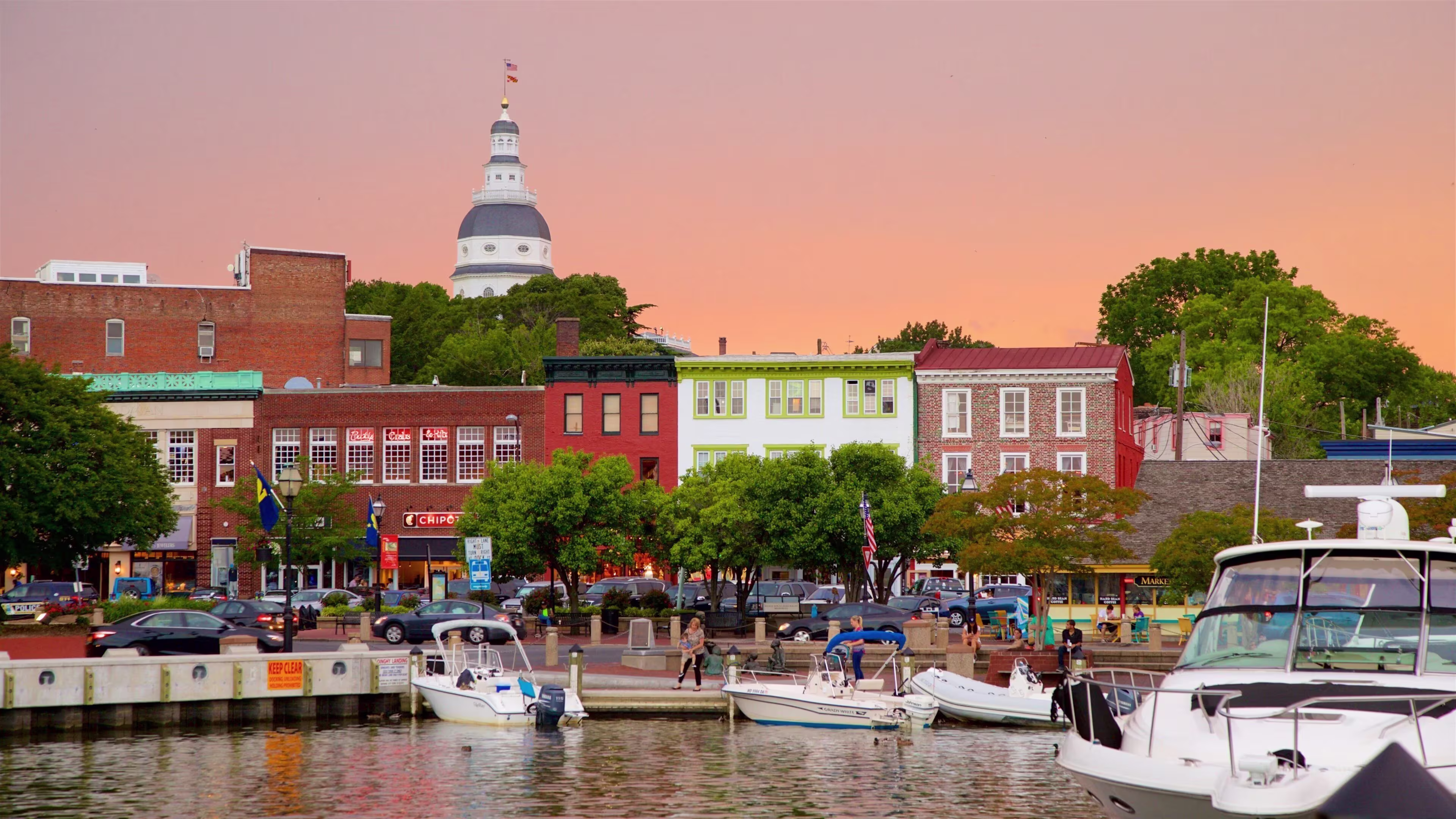 Waterfront view of Annapolis, Maryland at sunset with the State House dome, brick storefronts and boats moored at the harbor