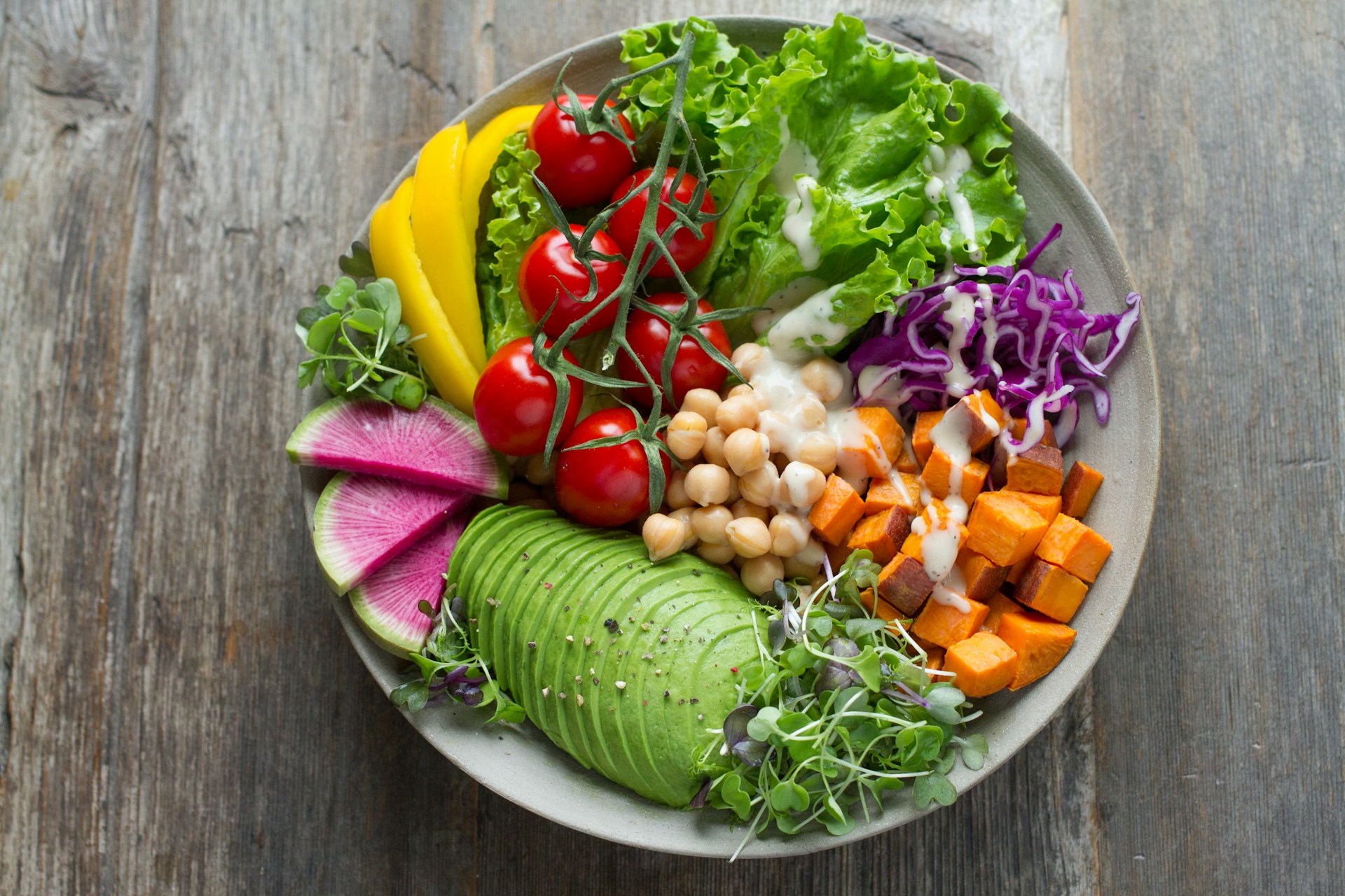Healthy grain bowl with avocado, chickpeas, cherry tomatoes, sweet potato, radish and greens on a rustic wood table
