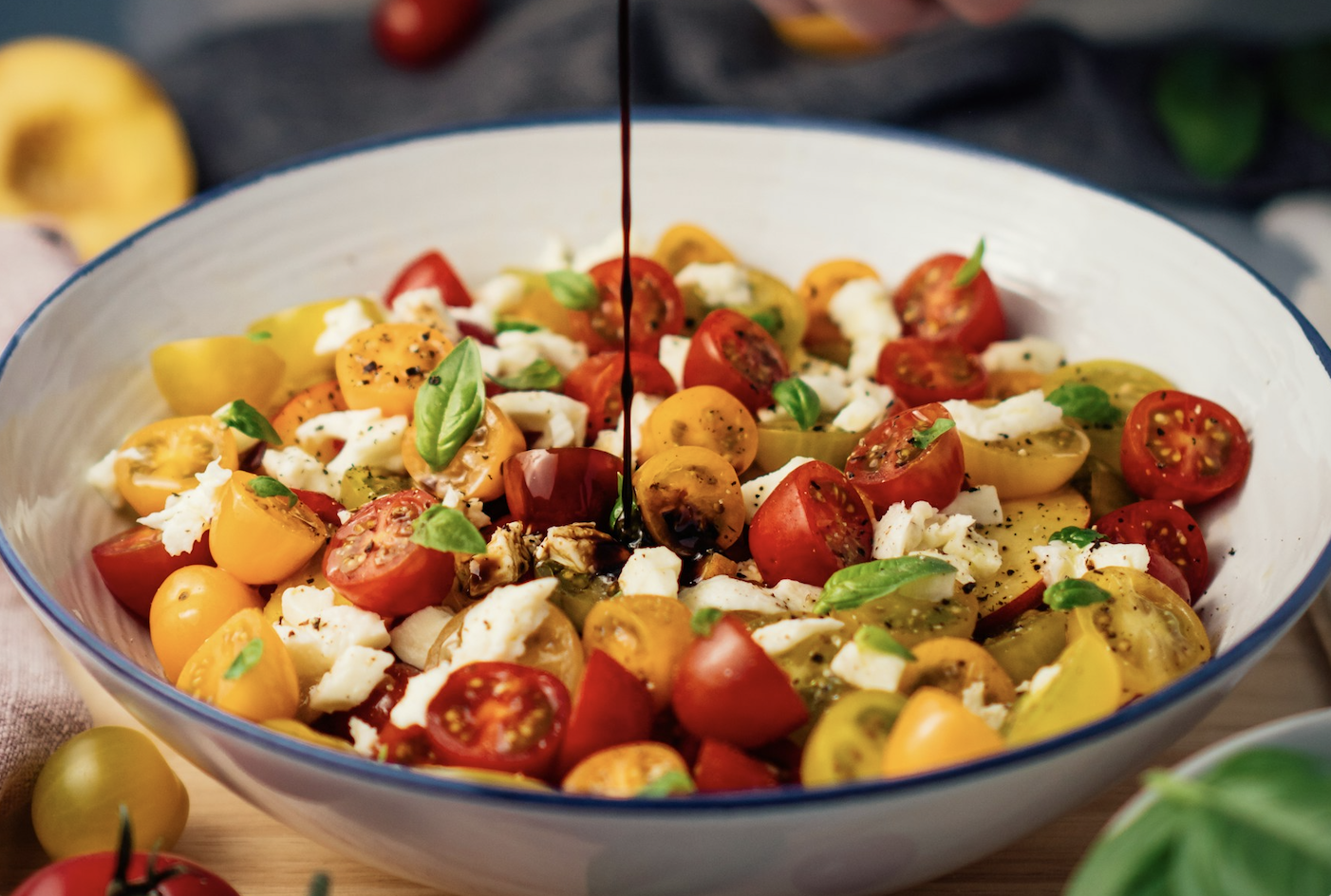 Caprese salad of red and yellow cherry tomatoes with fresh mozzarella and basil, drizzled with balsamic in a white bowl