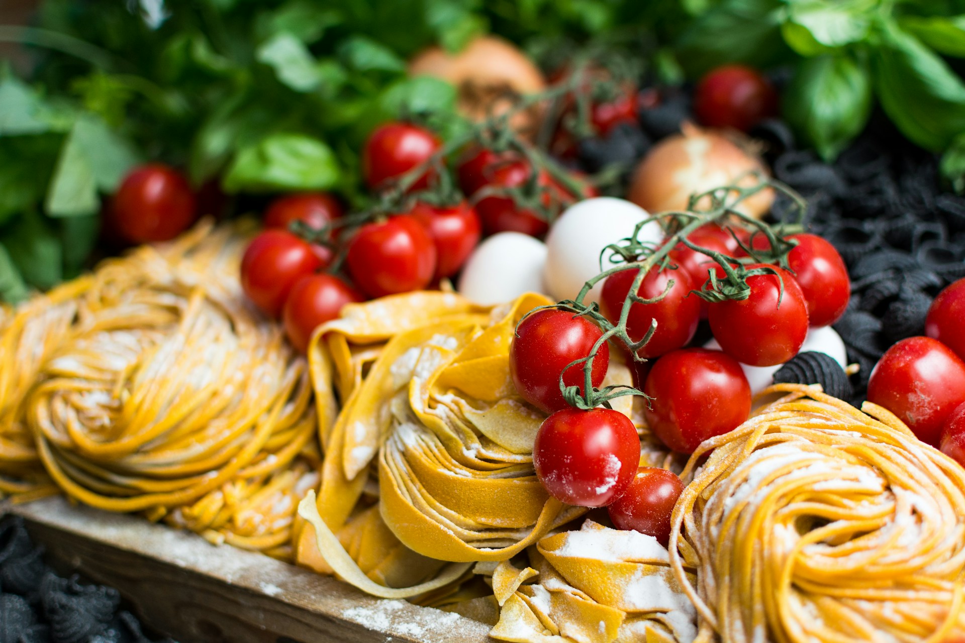 Fresh nests of yellow Italian pasta beside vine cherry tomatoes, basil, onions and eggs on a wooden surface
