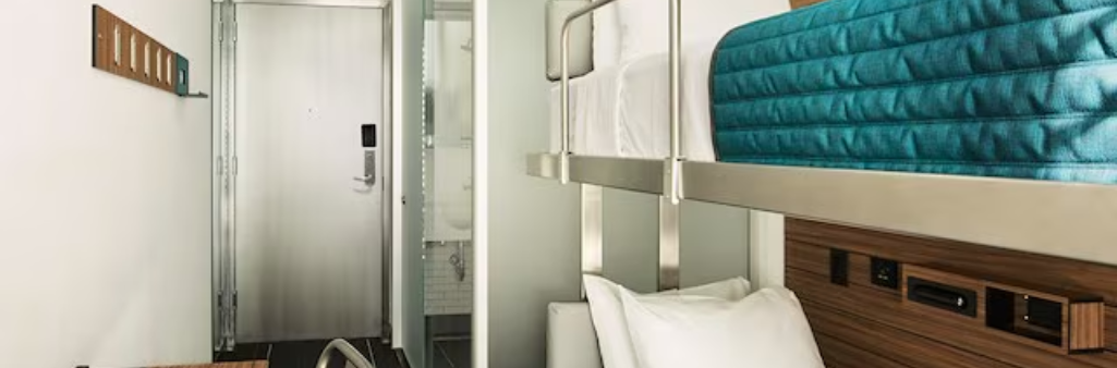 Modern hotel room with bunk beds, wood and metal decor, and a closed door to the bathroom.