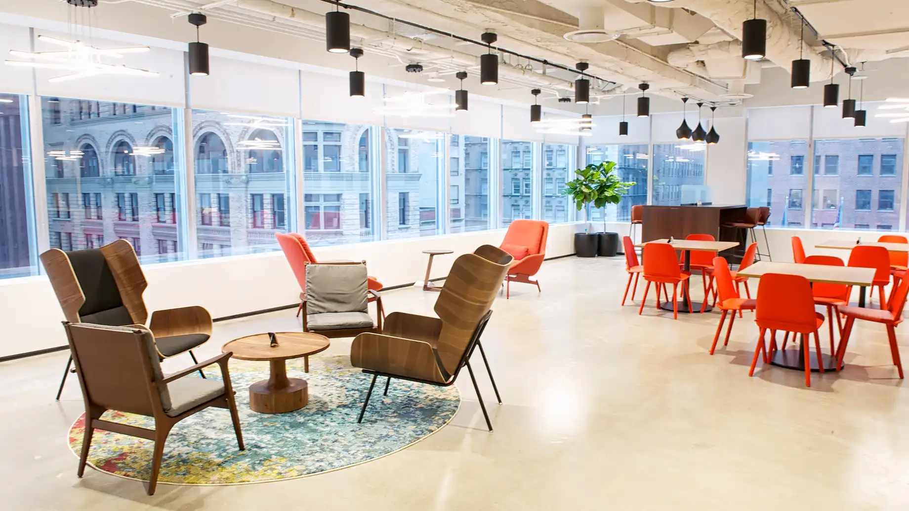 Lower Manhattan coworking lounge with mid-century armchairs, red chairs and tables, a patterned rug and skyline views