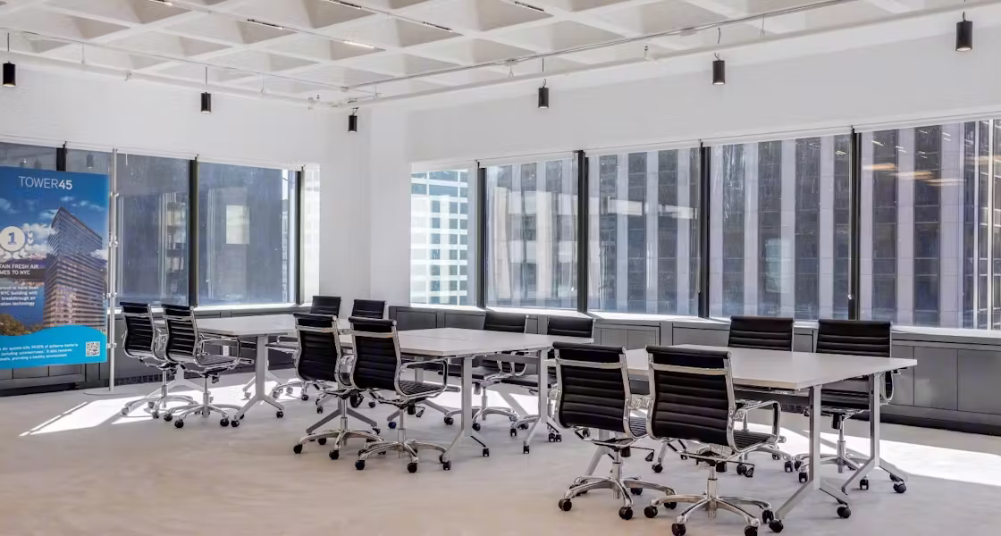 Coworking meeting room in Midtown Manhattan with white tables, black chairs and floor-to-ceiling windows over the city skyline