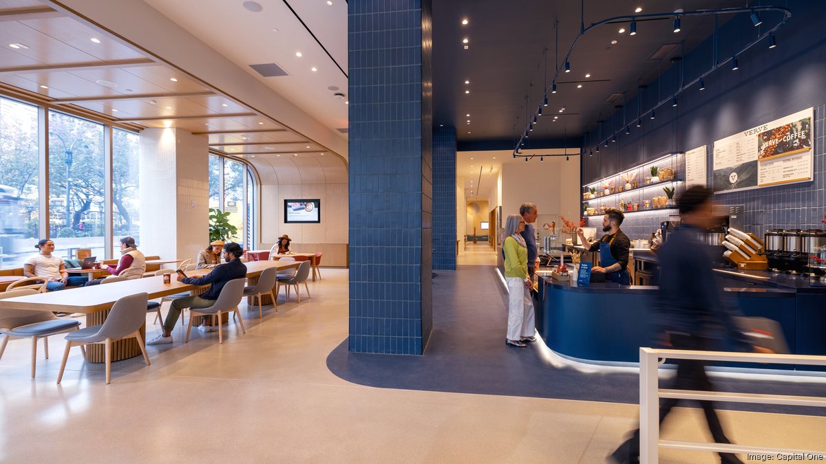 Capital One Cafe-style workspace lobby with communal tables, people working, a blue coffee counter and large windows