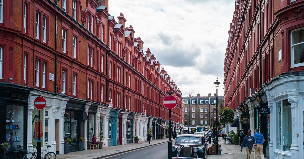 Central London street lined with red-brick mansion blocks, shops and a classic black car