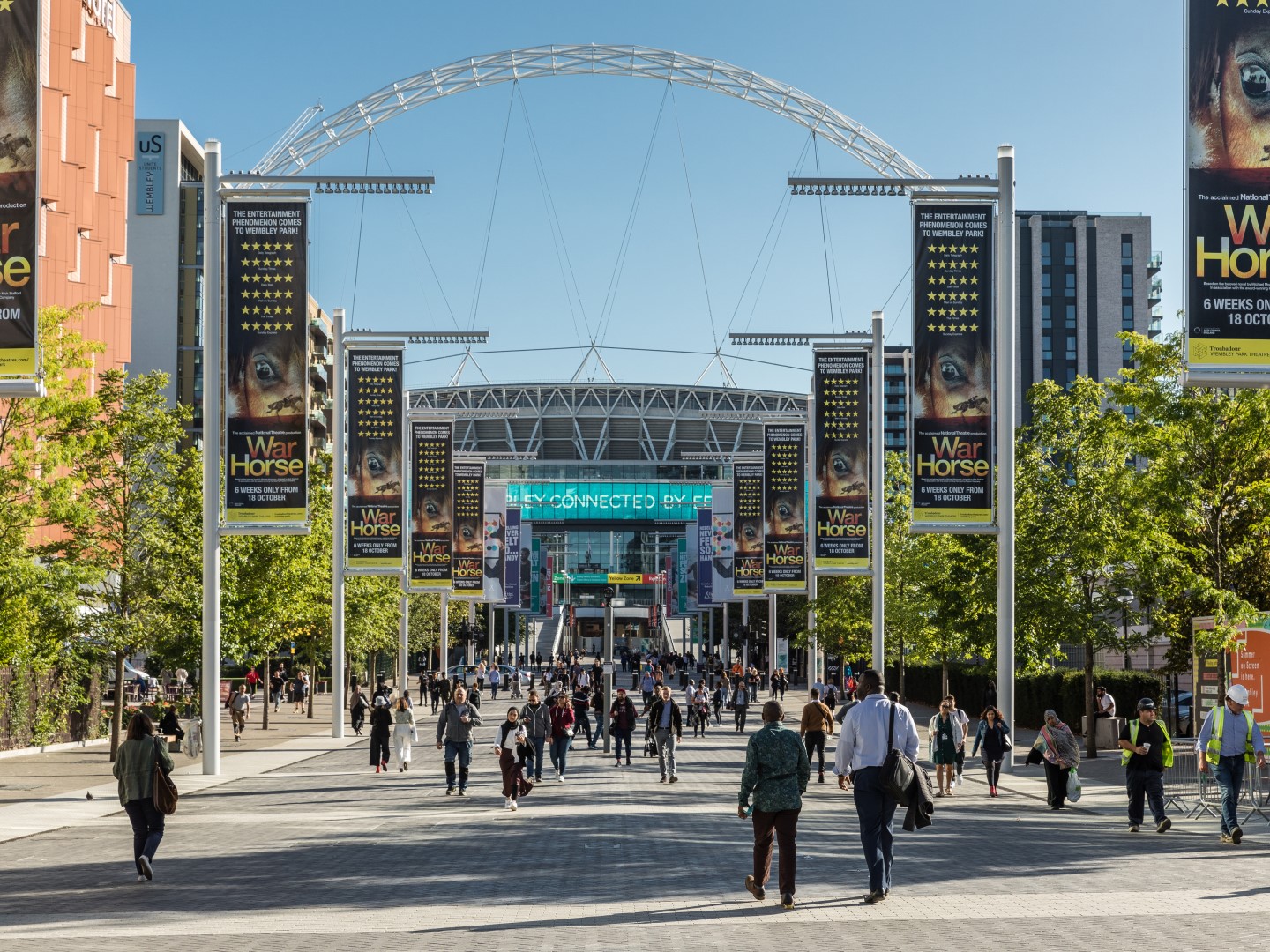 Crowds walking up Wembley Way toward the arched Wembley Stadium under a clear sky in London