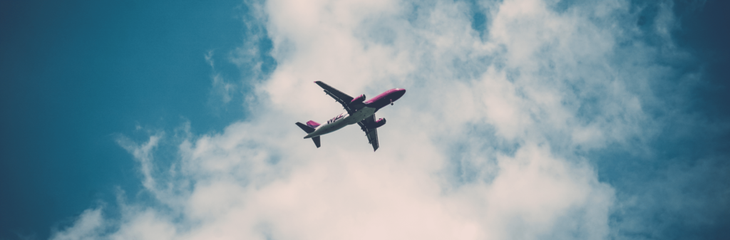 A commercial airplane flies overhead against a blue sky with scattered white clouds.