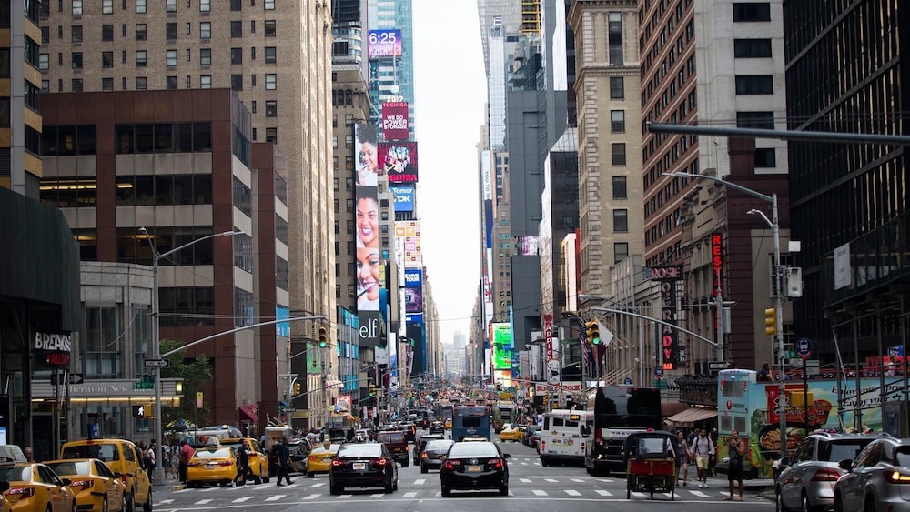 Busy city street with tall buildings, yellow taxis, cars, and people walking in New York City